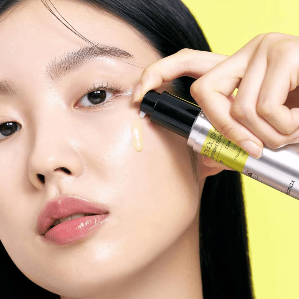 Model brengt The Vita-A Retinol Shot Tightening Serum van Tiam aan nabij het ooggebied, met focus op de glans van de huid en de gele consistentie van het serum.