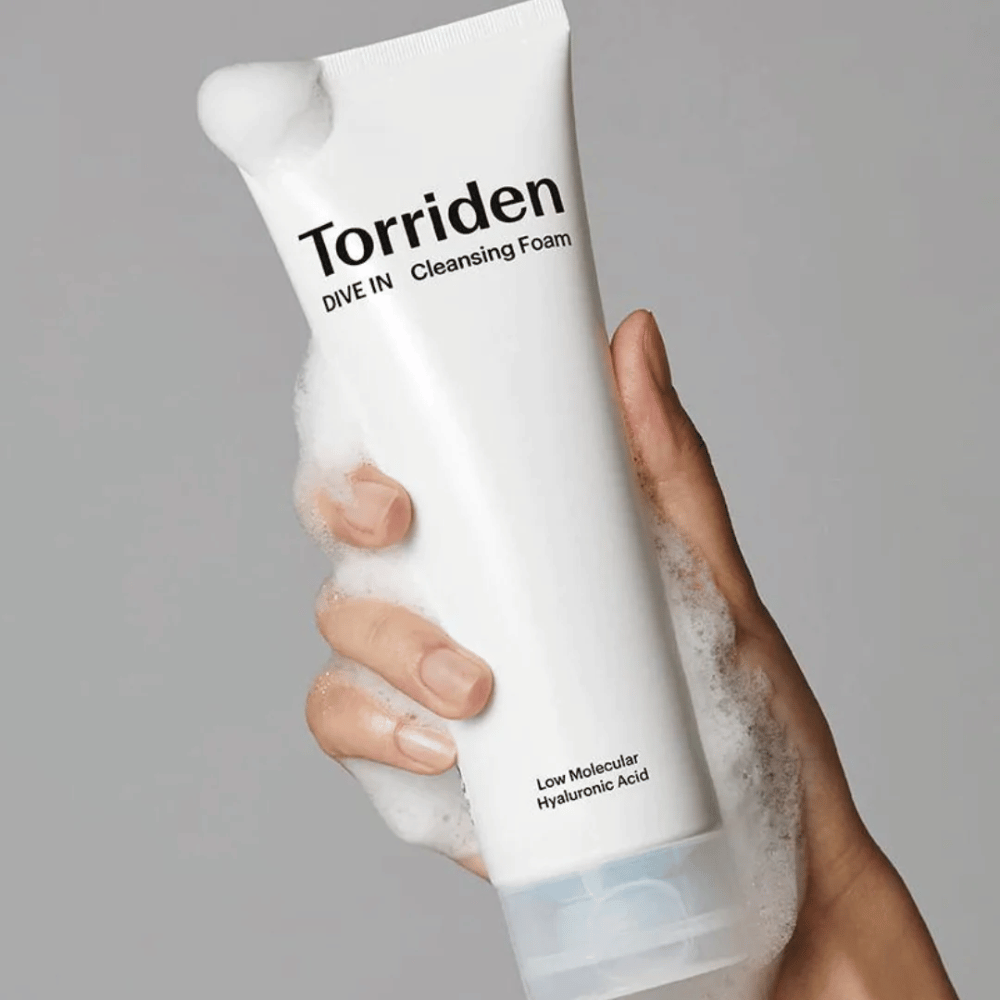 Een hand die een tube pH-gebalanceerde Torriden DIVE-IN Low Molecular Hyaluronic Acid Cleansing Foam 150ml vasthoudt.