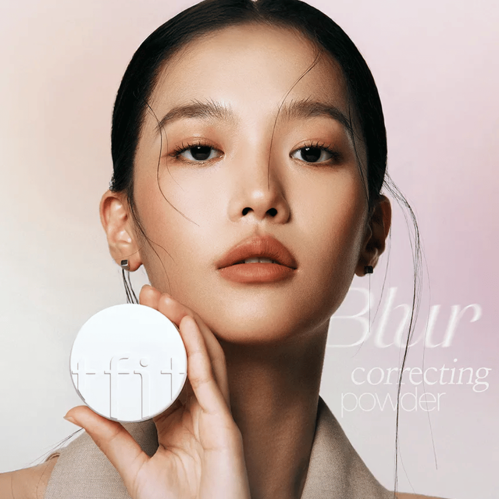 Vrouw met perfecte make-up houdt een ronde witte doos vast met TFIT-logo, met de tekst "Blur Correcting Powder" op de achtergrond.