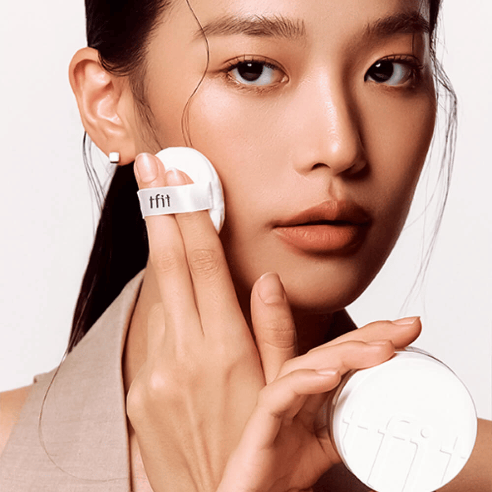 Vrouw brengt TFIT Translucent Set Finishing Powder #02 Skin Beige aan met een puff, houdt een witte poederdoos vast met TFIT-logo.
