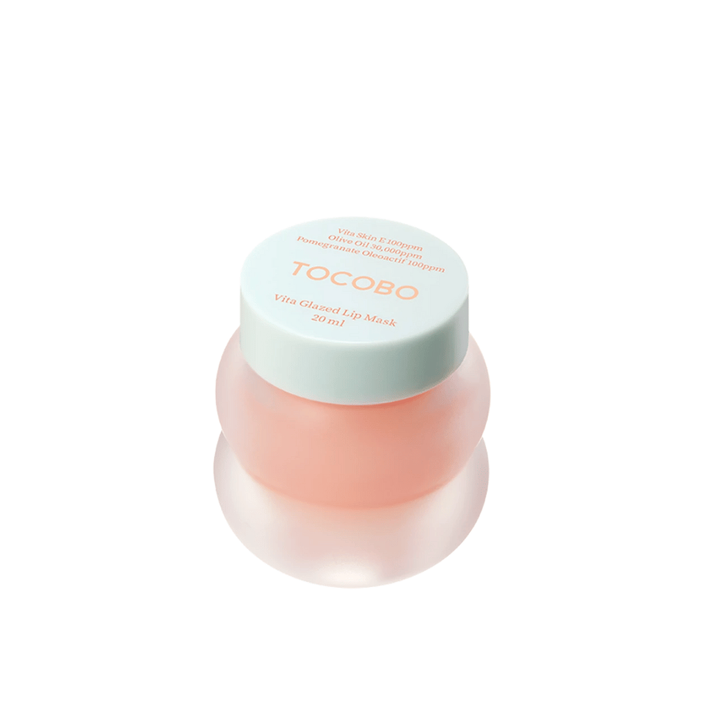 Een pot met "Vita Glazed Lip Mask" van Tocobo wordt getoond. De pot is rond en doorzichtig met een licht turquoise deksel. Het masker binnenin is lichtroze en ontworpen om de lippen te hydrateren en te verzorgen. Het product heeft een inhoud van 20 ml.
