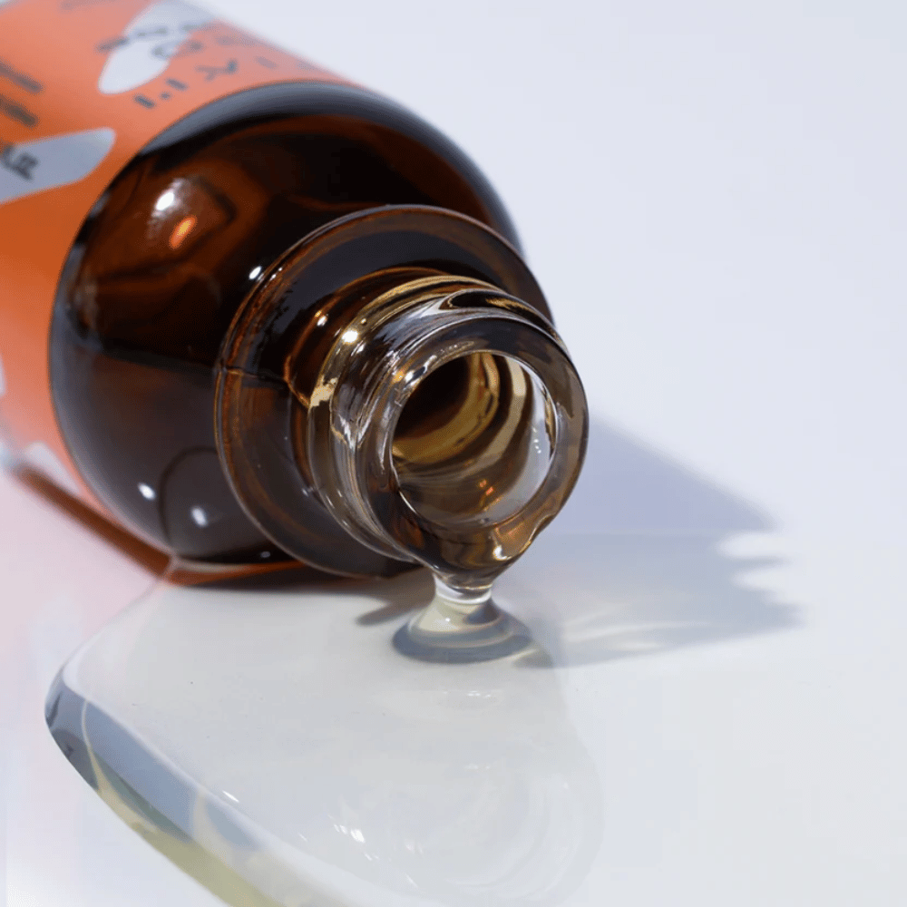 Close-up van TIA'M Vita C Source-serum dat uit een bruine glazen fles stroomt. De heldere formule van het serum benadrukt het geconcentreerde vitamine C-gehalte voor een stralende huid.