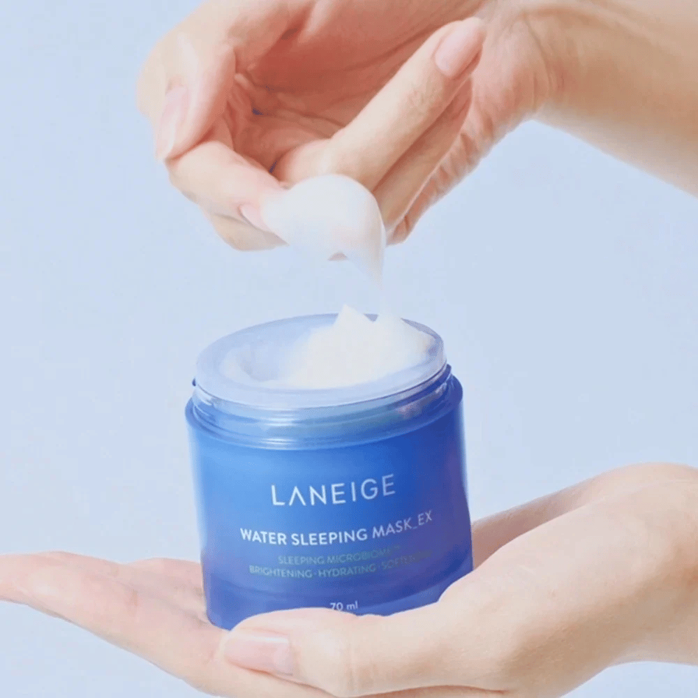 Een hand schept LANEIGE Water Sleeping Mask uit een blauwe pot, met de focus op de gelachtige consistentie tegen een lichtblauwe achtergrond.
