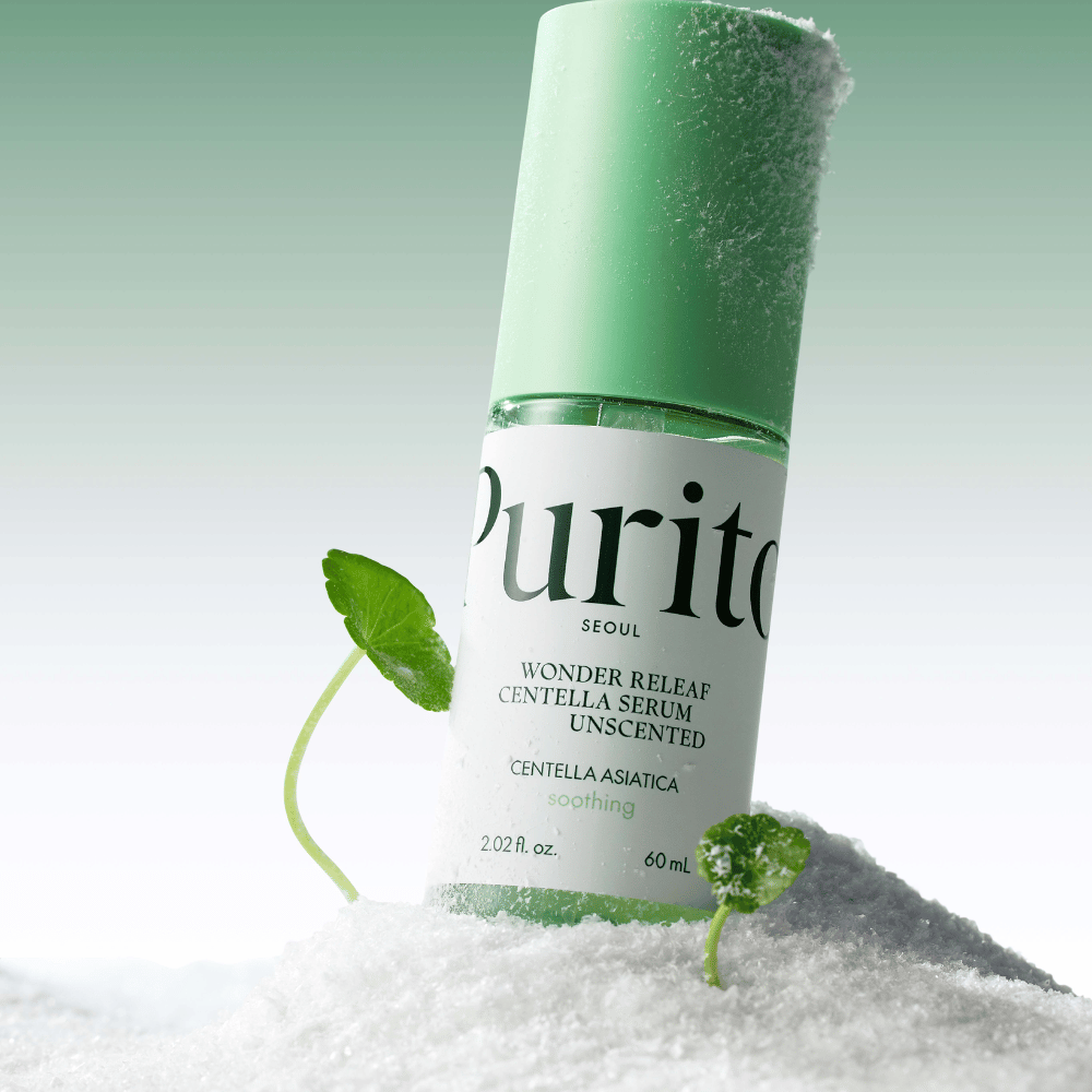 Fles met Purito Centella Serum ligt in de sneeuw, groene bladeren zijn zichtbaar, tegen een zachte groene achtergrond.