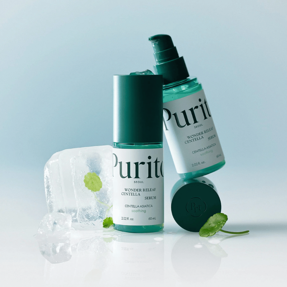 Twee flessen van Purito Wonder Releaf Centella Serum, één staand en één liggend, omgeven door ijsblokjes met centellabladeren erin en een los blad op een lichtblauw oppervlak.