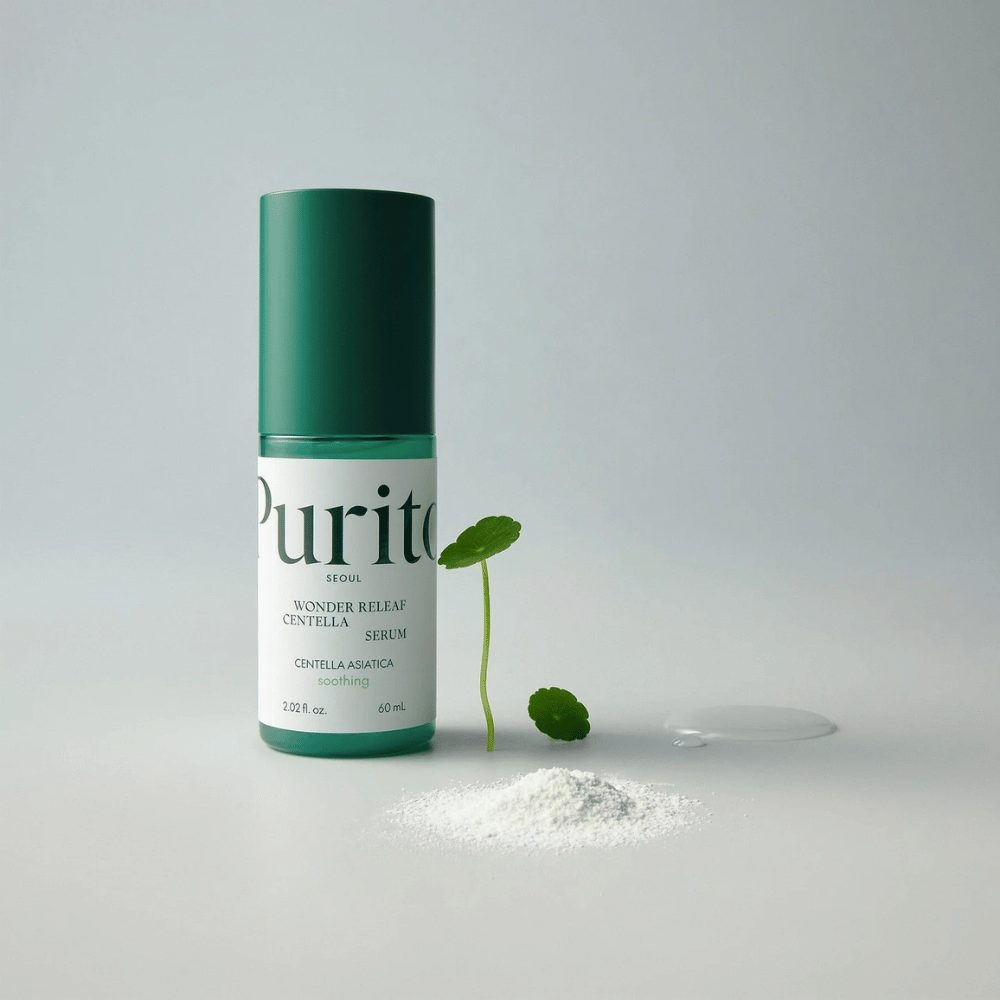 Groene fles van Purito Wonder Releaf Centella Serum 60 ml staat op een witte ondergrond, omringd door centellabladeren, een transparante serumdruppel en een klein wit poeder.