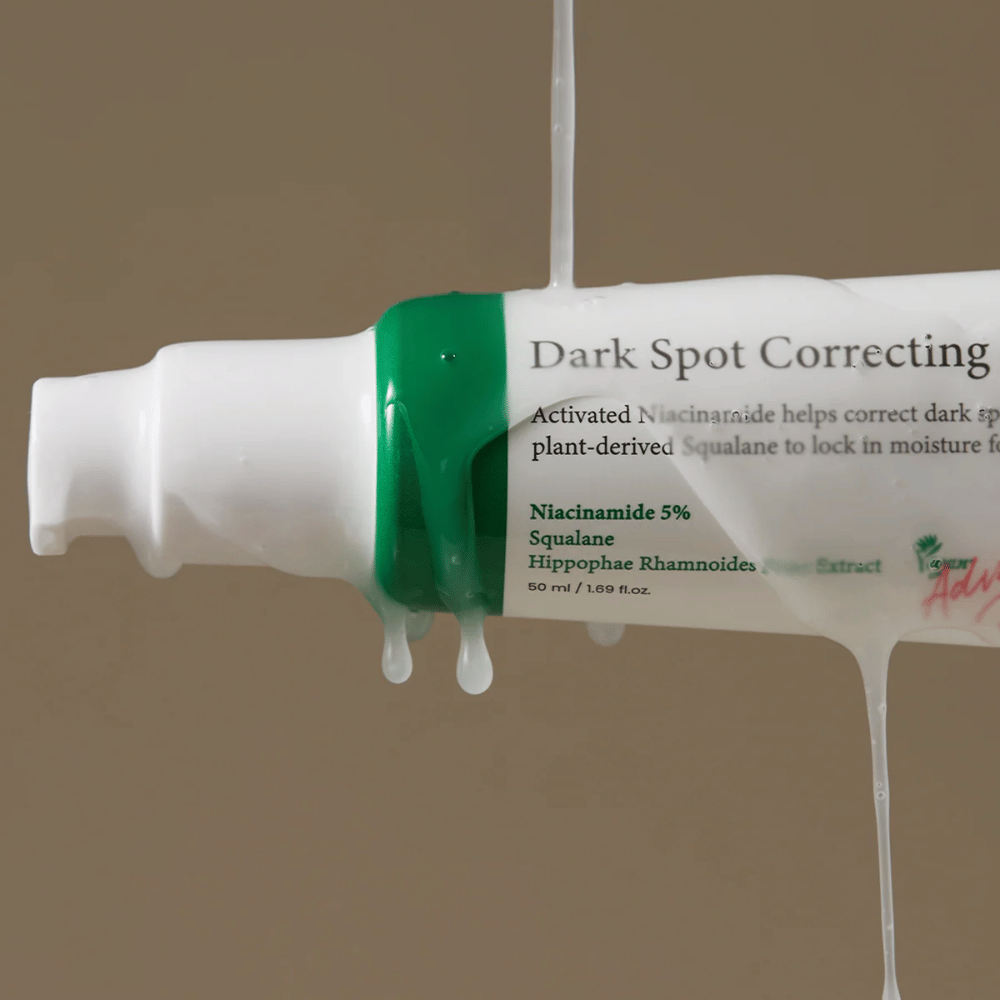 Close-up van een pompflacon van Axis-Y Dark Spot Correcting Glow Serum met witte verpakking en groene dop, bedekt met stromende transparante vloeistof.