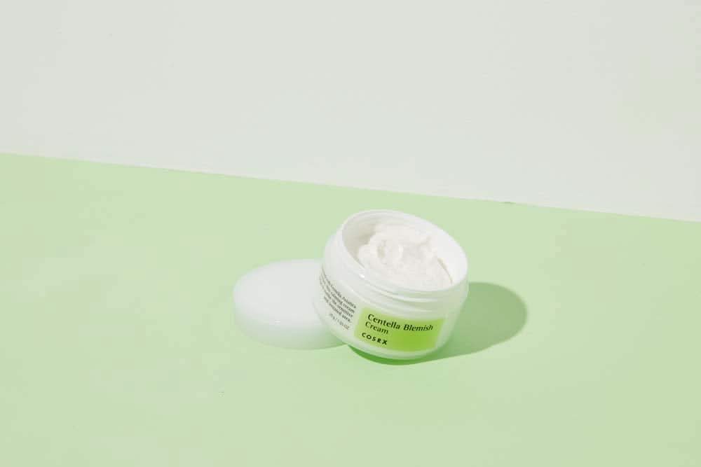 Een pot COSRX Centella Blemish Cream 30ml die op een groen oppervlak staat.