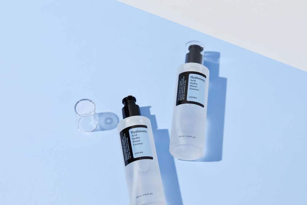 COSRX:s Hyaluronic Acid Hydra Power Essence 100ml biedt hydraterende voordelen op een blauwe oppervlakte.
