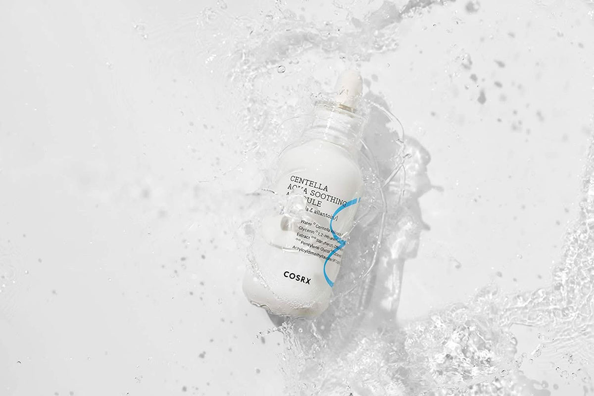 Een fles COSRX Centella Aqua Soothing Ampoule 40ml die spettert op een wit oppervlak, vermindert roodheid en biedt kalmerende hydratatie.