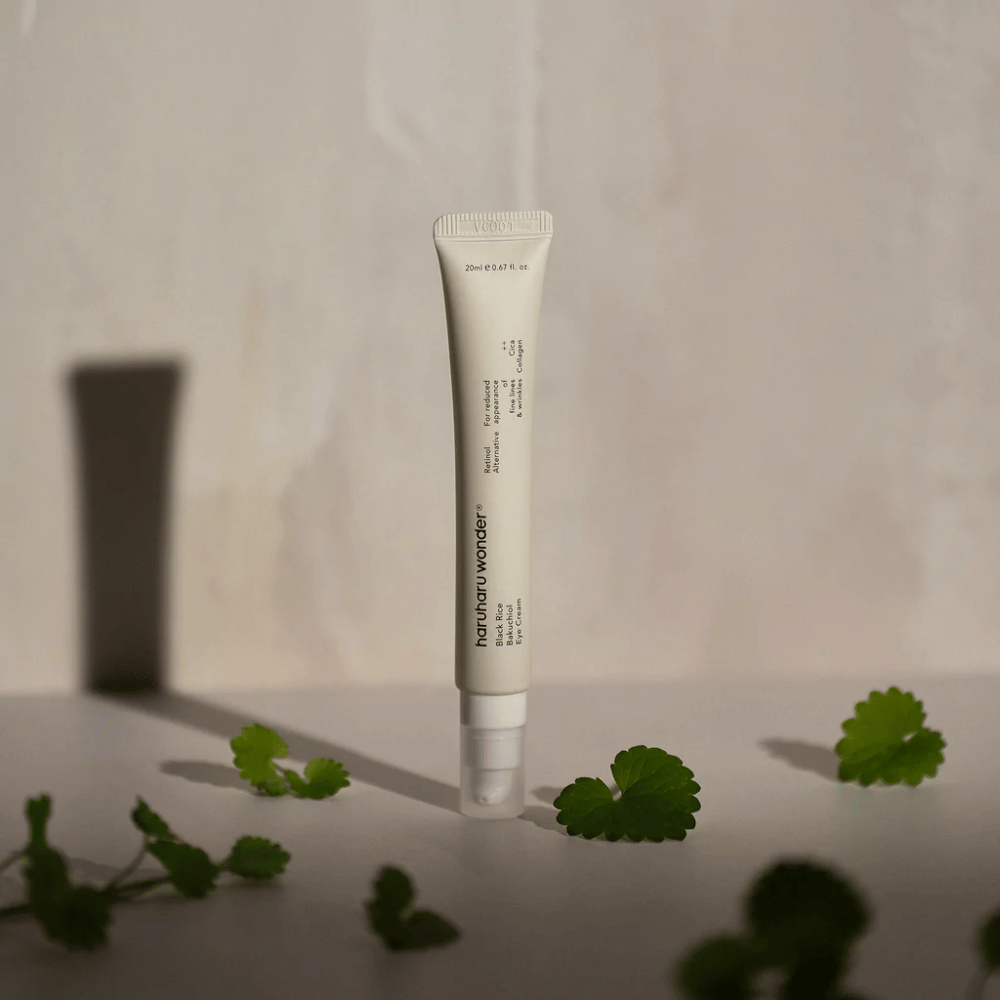 Een tube Haruharu Wonder Black Rice Bakuchiol Eye Cream 20ml omgeven door groene bladeren, gericht op de zichtbaarheid van rimpels en fijne lijntjes.