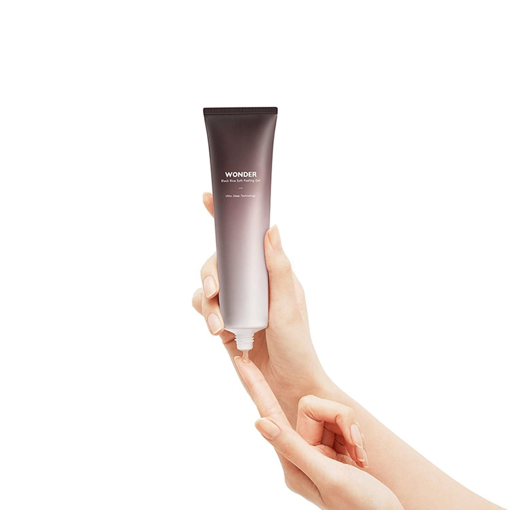 De hand van een vrouw die een tube Haruhuru Wonders Black Rice Soft Peeling Gel 100 ml vasthoudt op een witte achtergrond.