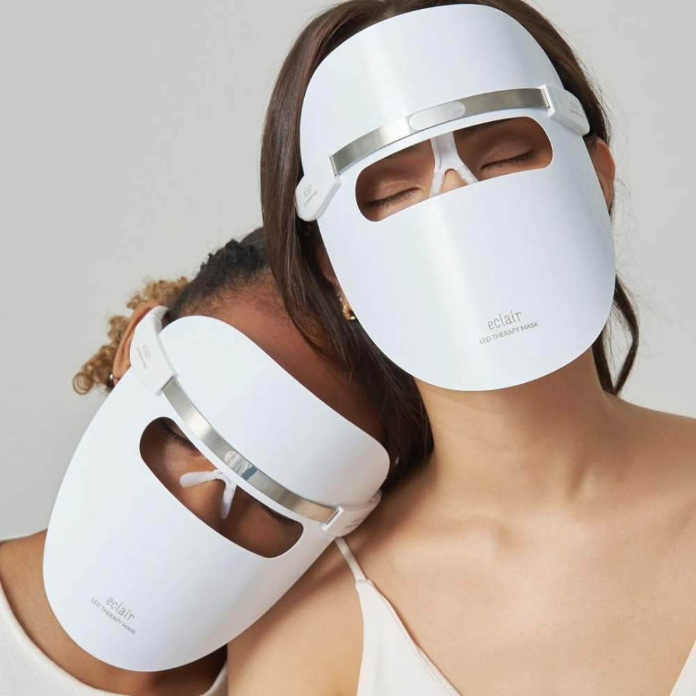 Twee vrouwen die witte maskers dragen demonstreren ECLAIR LED Therapy Mask voor huidtintverbeteringen.