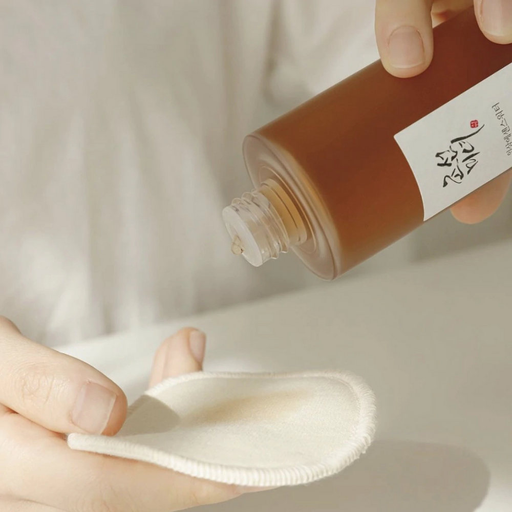 Een persoon die Beauty of Joseon Ginseng Essence Water 150ml op een doek aanbrengt om droge huid aan te pakken en talgproductie te verminderen.