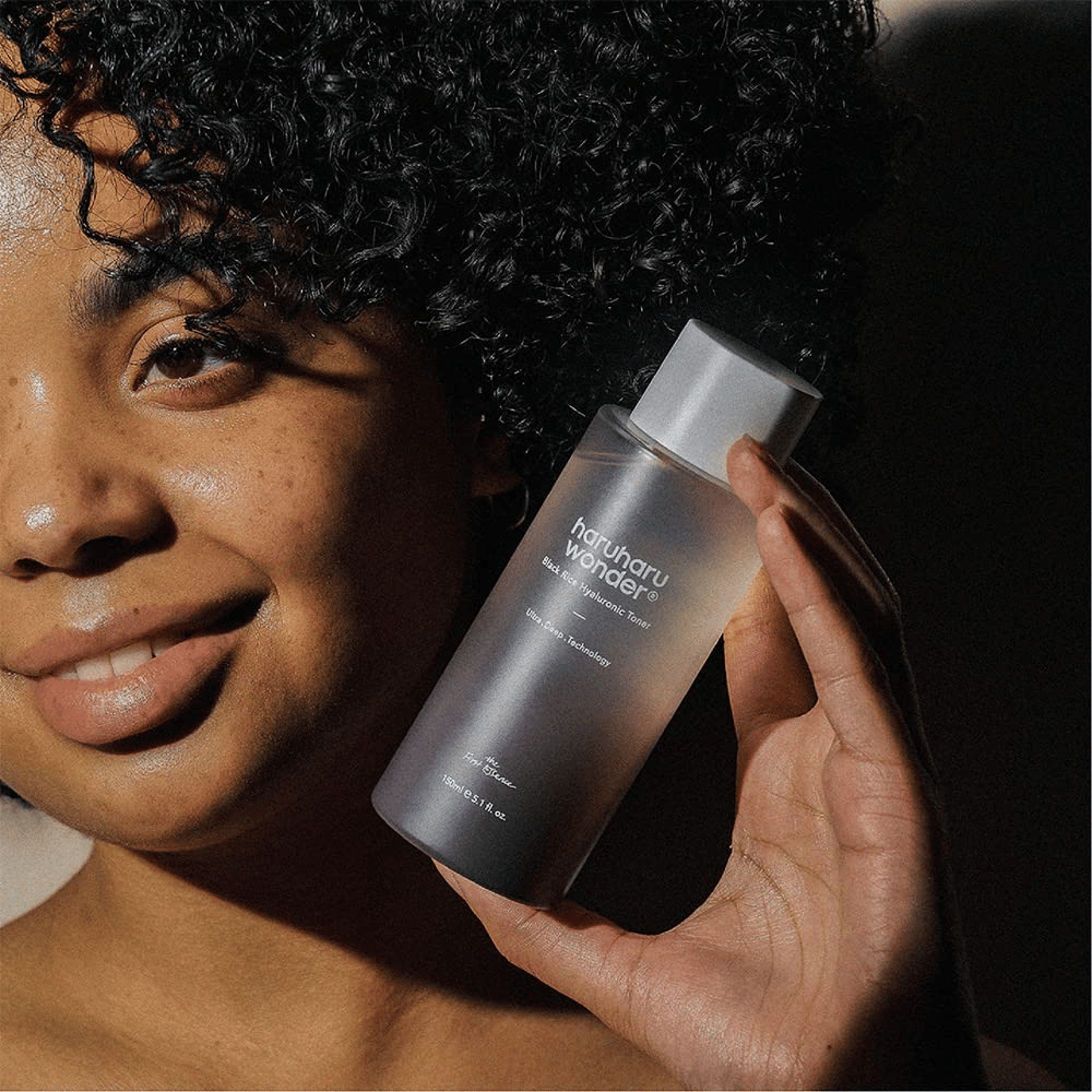 Een vrouw die een fles Haruharu Wonder Black Rice Hyaluronic Toner Original 150ml omhoog houdt.