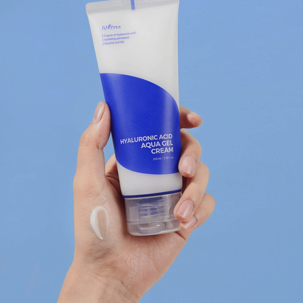 Een hand die een tube Isntree Hyaluronic Acid Aqua Gel Cream 100ml vasthoudt op een blauwe achtergrond.